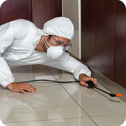 Technician in a protective suit applying treatment along a floor